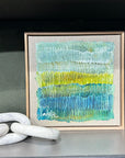 Original artwork by natalie Uhrik measuring 30cm square.  Framed in tasmanian oak frame. textural and featuring a colour palette of blue and greens with hues of gold
