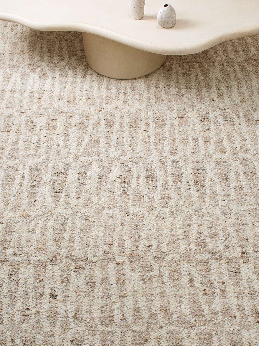 Close-up of a textured beige carpet with a white chair leg and small decorative item.