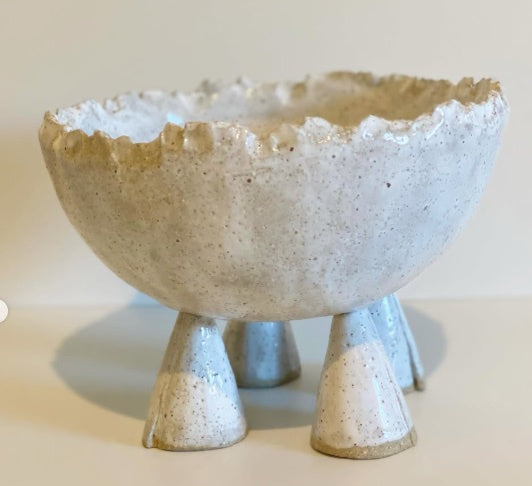 Ceramic bowl with textured surface and four small legs on a plain background