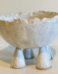 Ceramic bowl with textured surface and four small legs on a plain background
