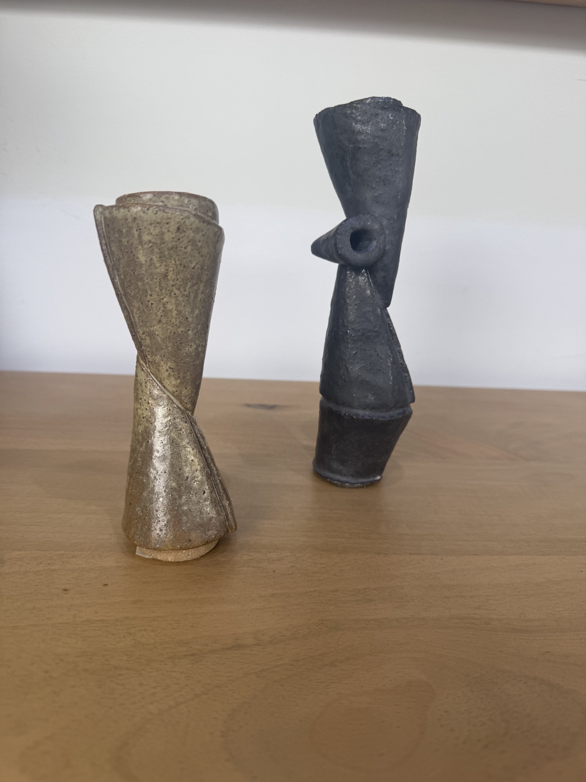 Two ceramic sculptures on a wooden surface with a white background
