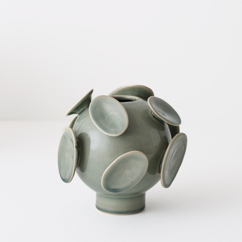 Green ceramic vase with circular disc design and  has a shiny glaze
